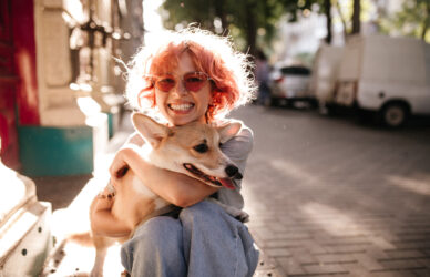happy-curly-woman-jeans-smiles-sincerely-hugs-corgi-dog