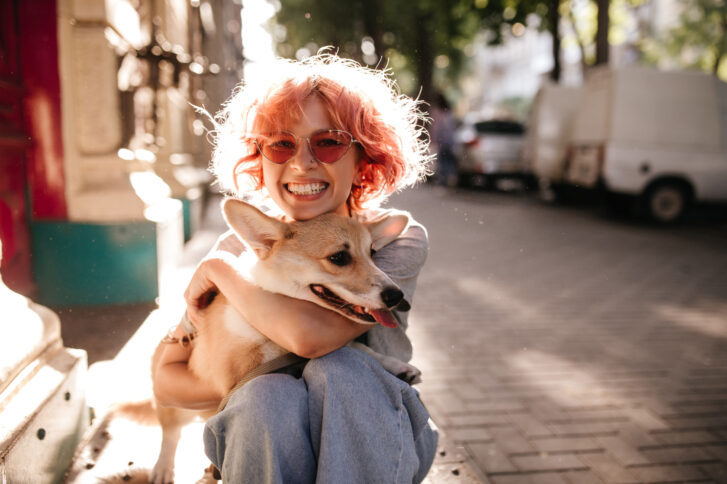 happy-curly-woman-jeans-smiles-sincerely-hugs-corgi-dog